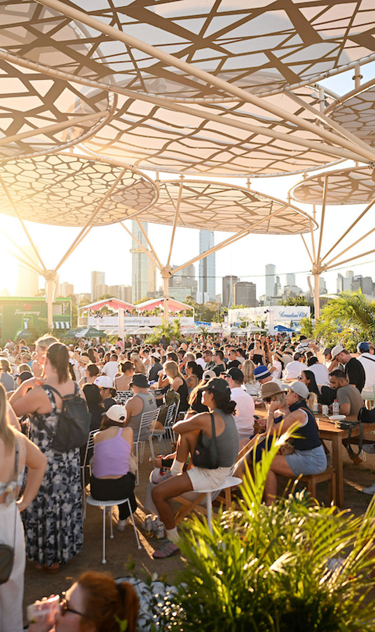 Crowd watching sports on big screens at venue enjoying food and drinks in the afternoon sun