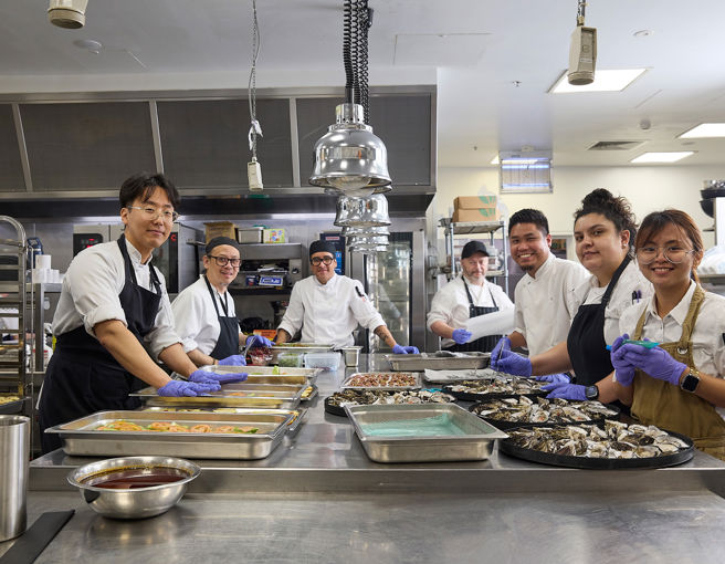 Group of chefs smiling at camera in commercial kitchen whilst prepping