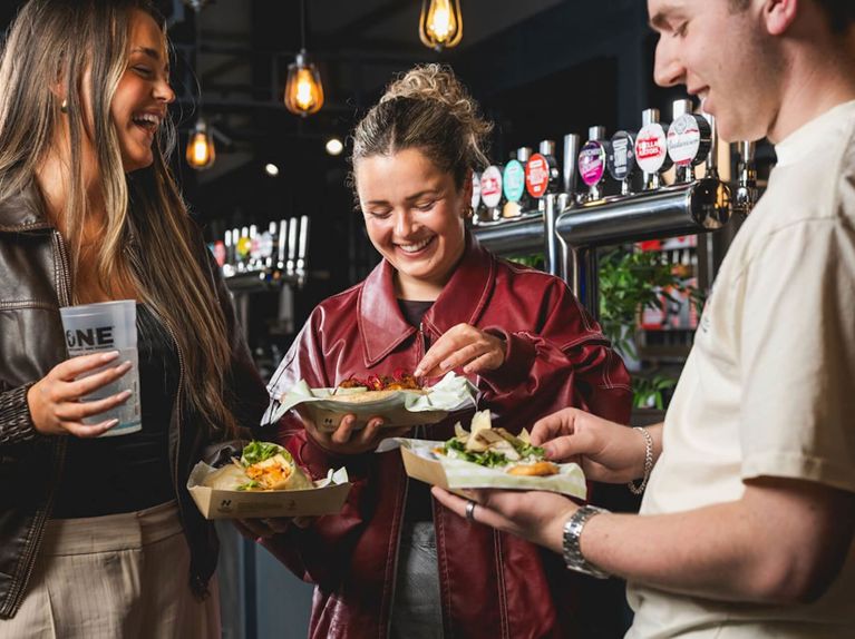 Smiling and laughing guests holding burgers and drinks at a bar
