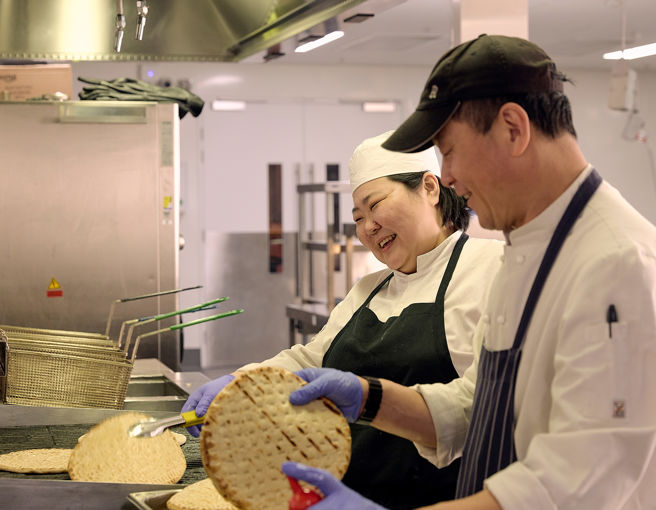 Two chefs laughing and cooking together in commercial kitchen